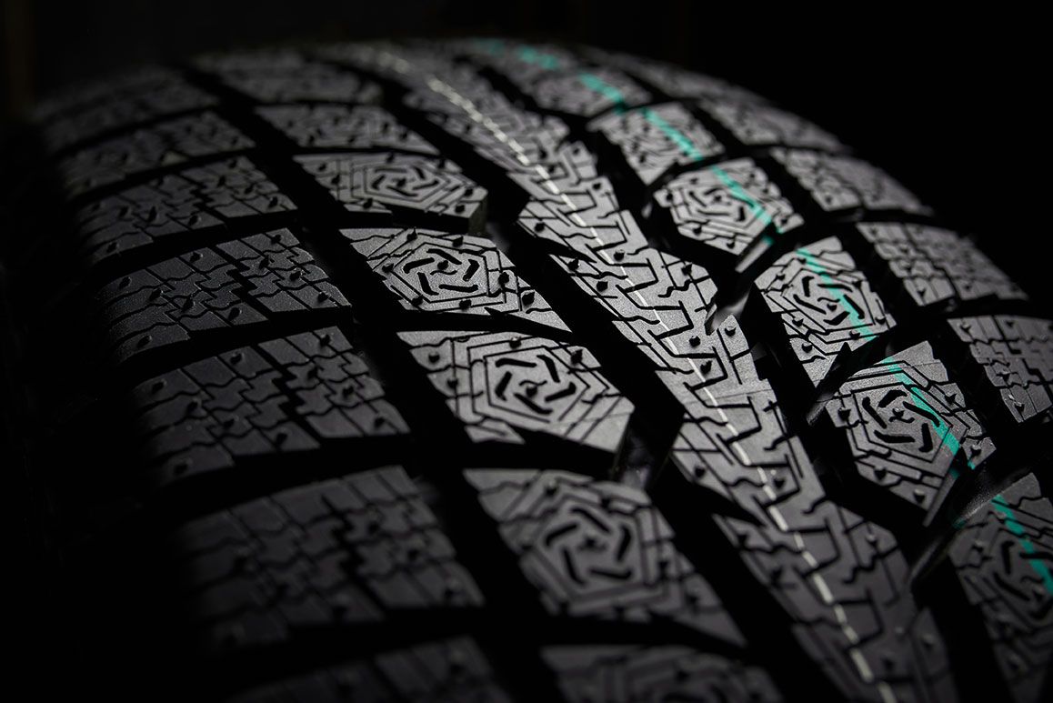 Close-up of a black tire tread with detailed patterned grooves and a few teal highlights