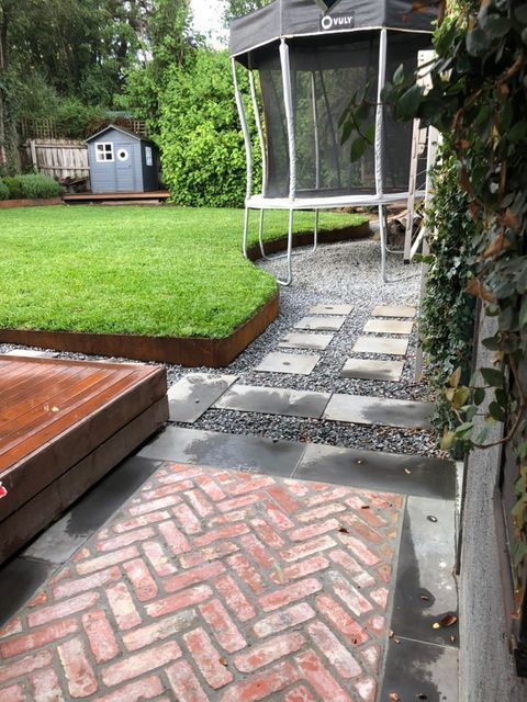 Backyard with green grass, stone path, brick patio, and trampoline.