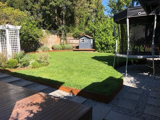 Backyard with green lawn, small wooden playhouse, and pergola.