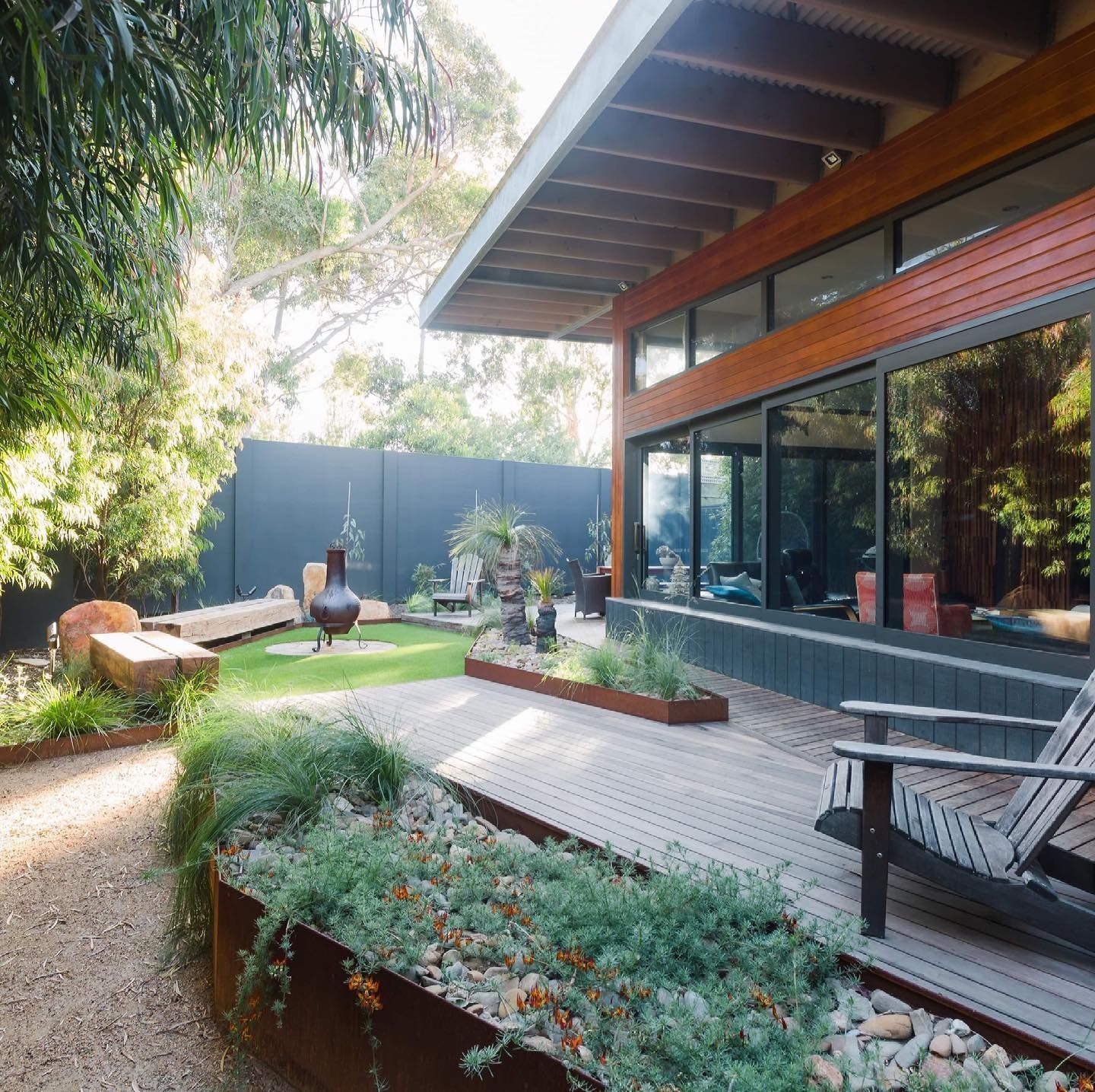 Patio with modern home, wooden deck, landscaping with greenery, lounge chair.