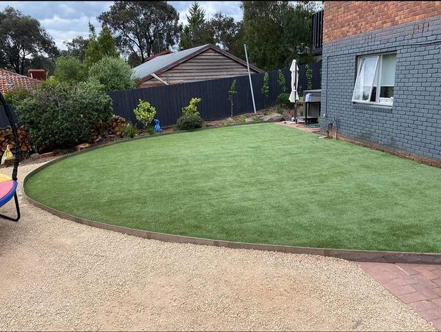 Lawn edged with wooden border, gravel path, and brick house.