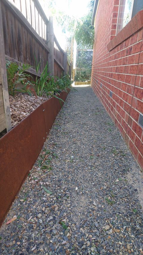 Gravel path between a brick wall and a fence, with a rusted metal border and some greenery.