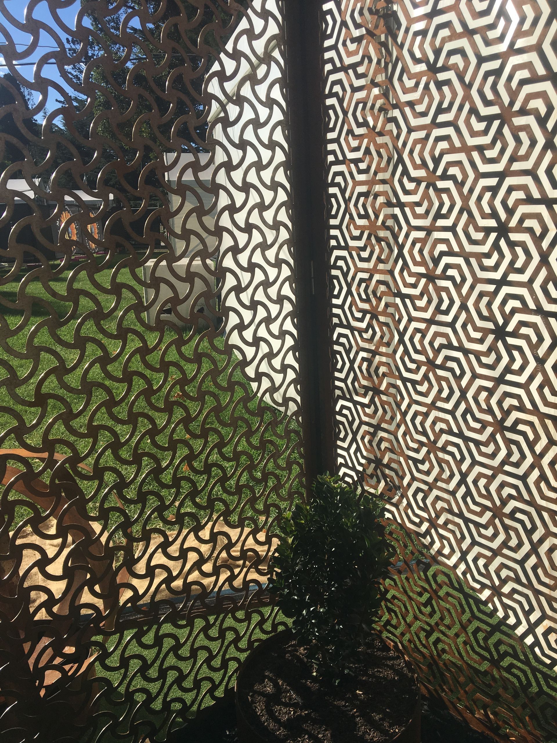 Camouflage netting with geometric and organic patterns hangs, partially obscuring a bush and view of green grass.