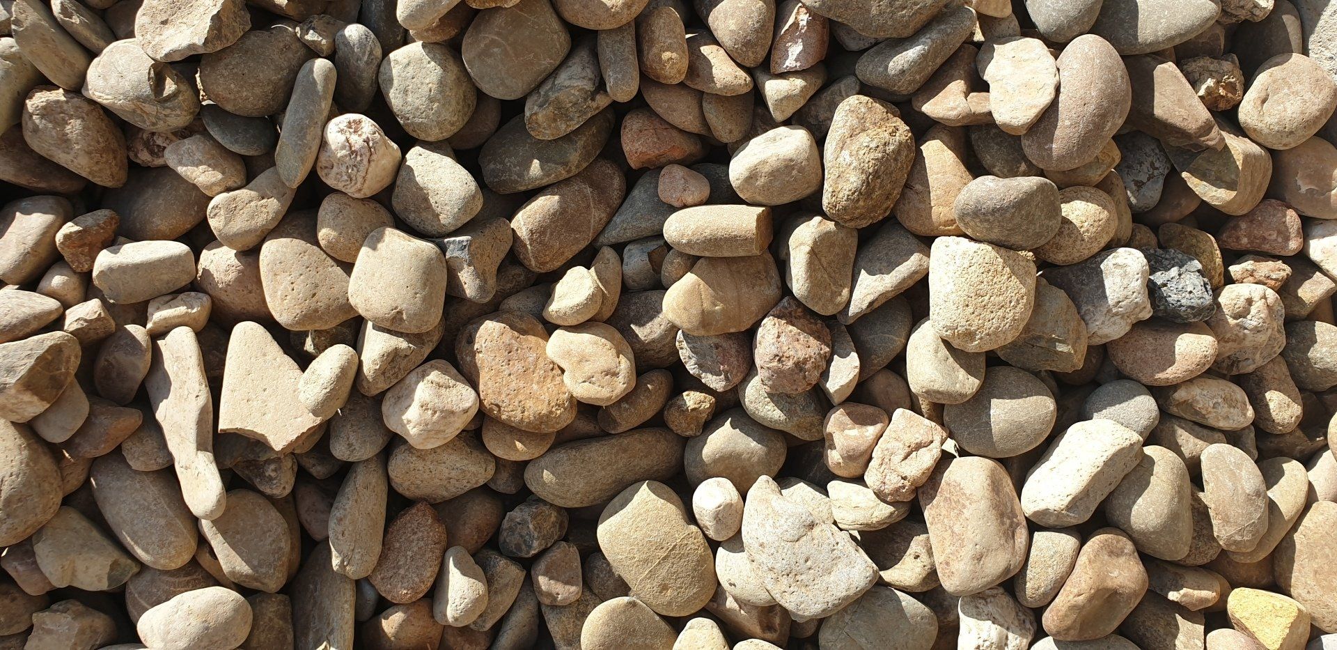 Close-up of a pile of small, smooth, beige and brown river rocks.