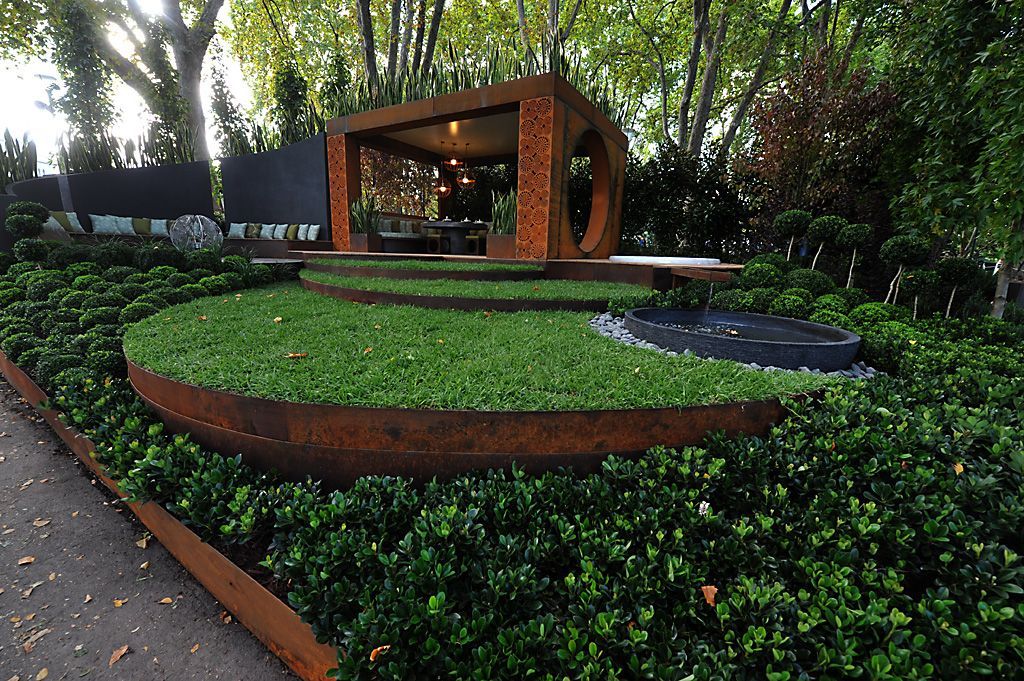 A modern garden with a rusted metal structure over a green grass area.