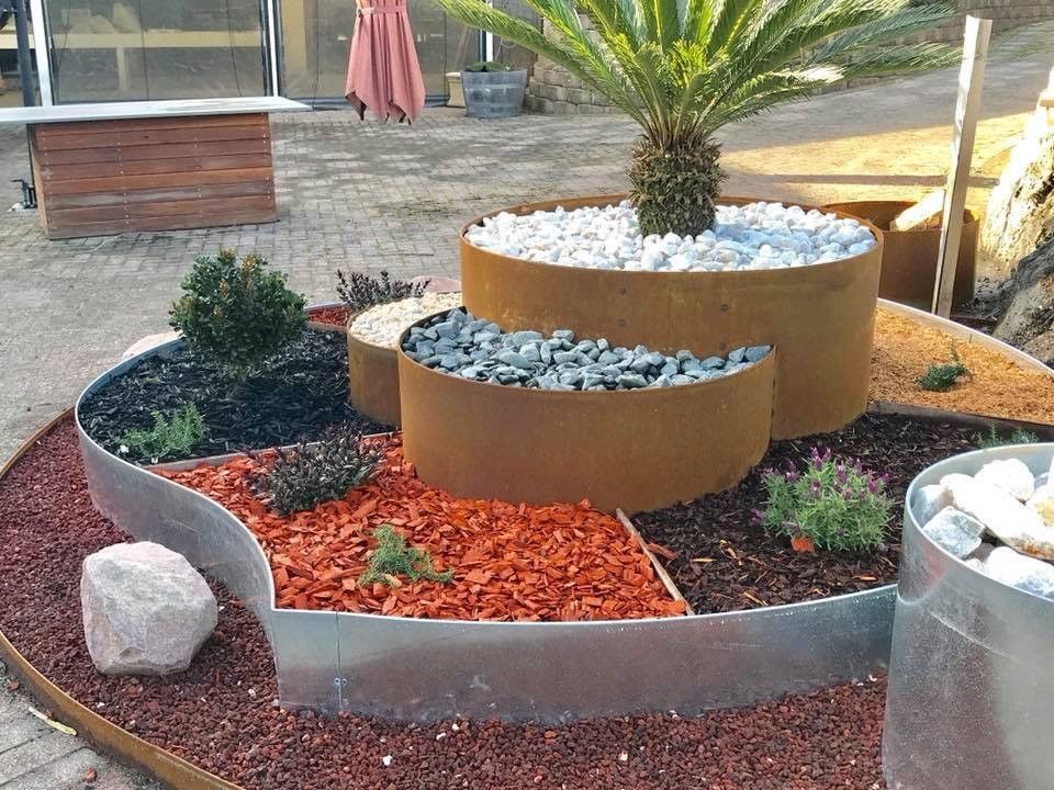 Tiered garden bed with rusty metal rings, holding plants and various colored stones.