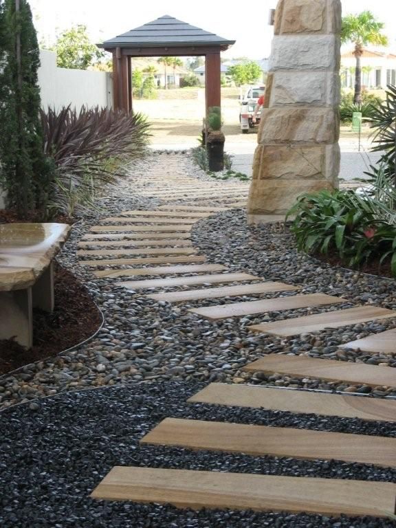 Stone path with wooden steps through dark gravel, leading to a wooden gate and a building entrance.