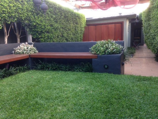 L-shaped concrete bench with a wooden seat, lush green lawn, and hedge backdrop.
