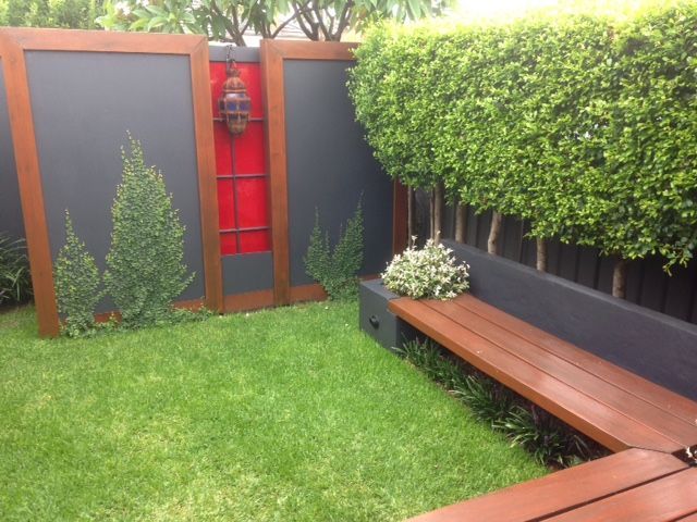 Small backyard with green grass, wooden bench, and gray and red decorative panels.