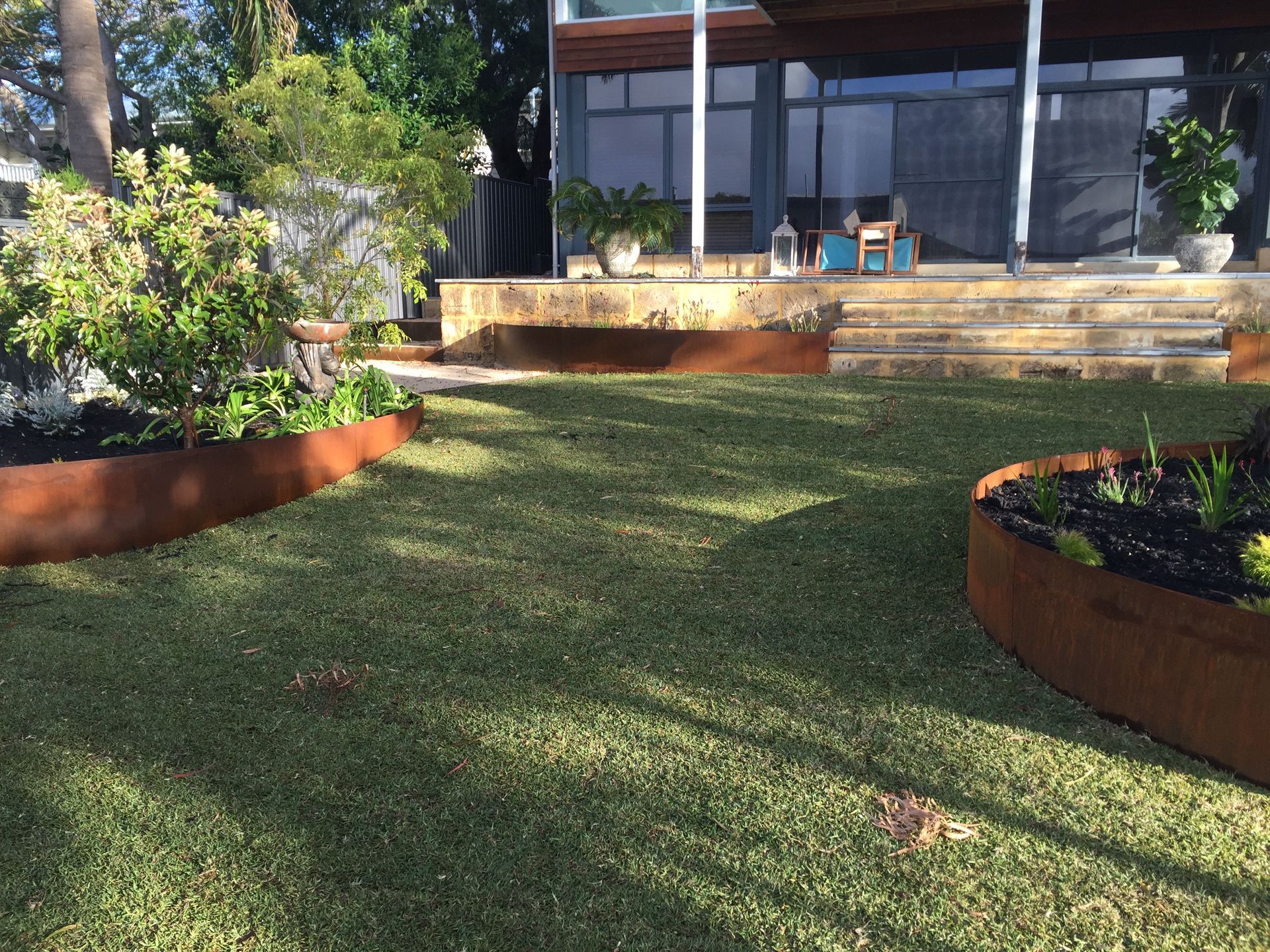 Lawn with rusted metal edging, plants, and a house with a porch.