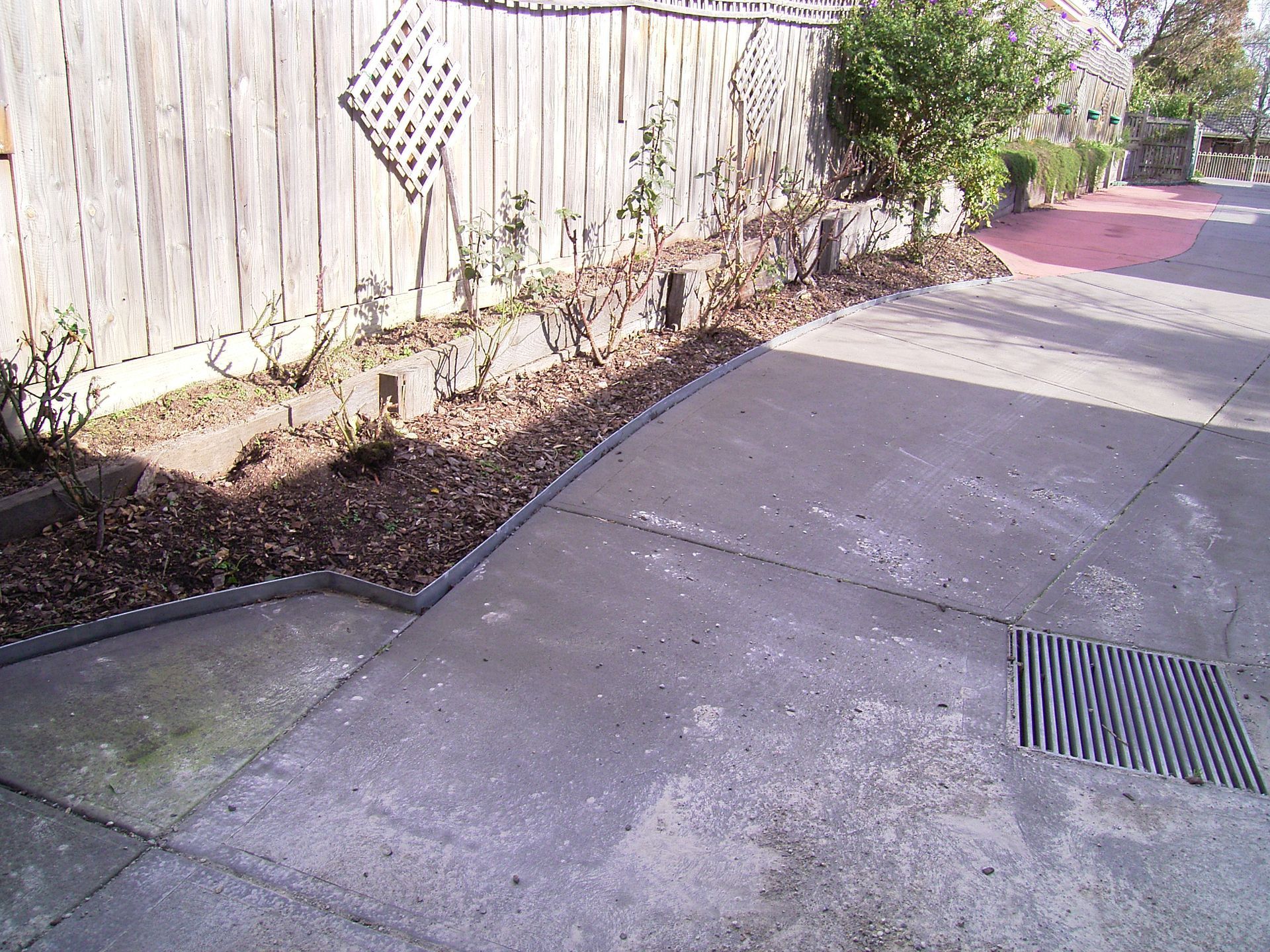 Concrete driveway borders a flower bed next to a wooden fence.