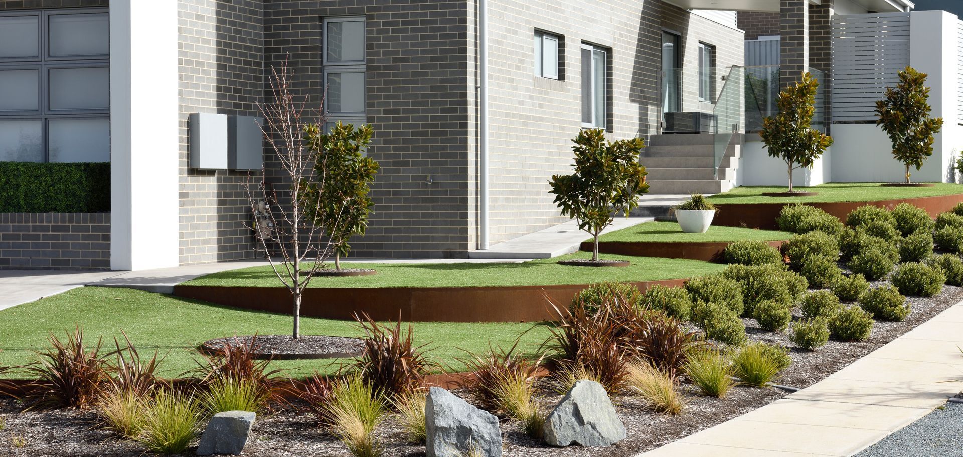 Modern home with tiered landscaping featuring small trees, shrubs, and ornamental grasses.