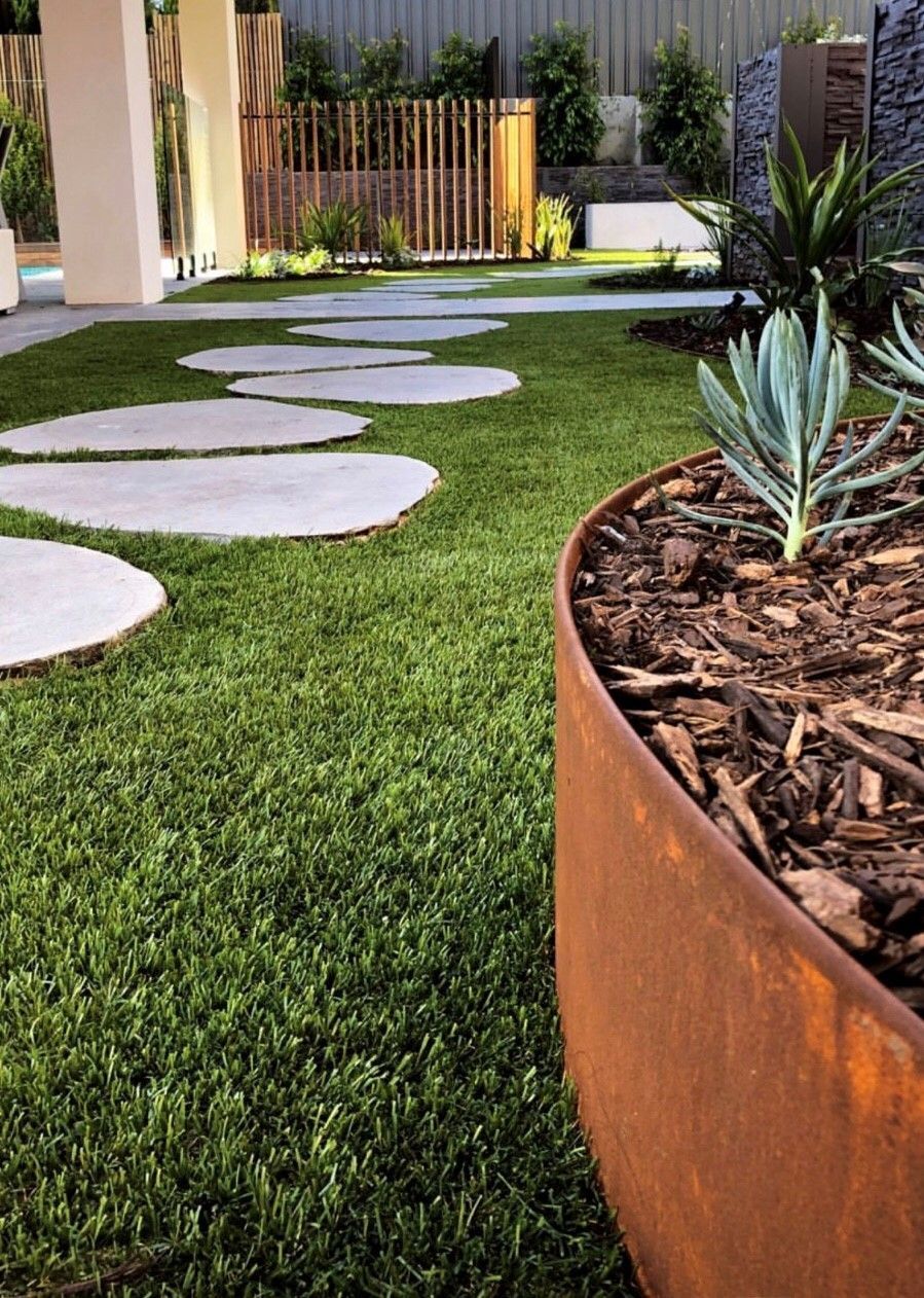 A curving corten steel planter with succulent plants, pathway of stepping stones, green grass.