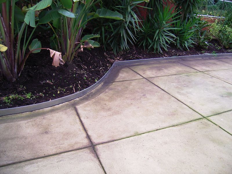 Concrete patio with garden bed, edged with metal. Plants are visible.