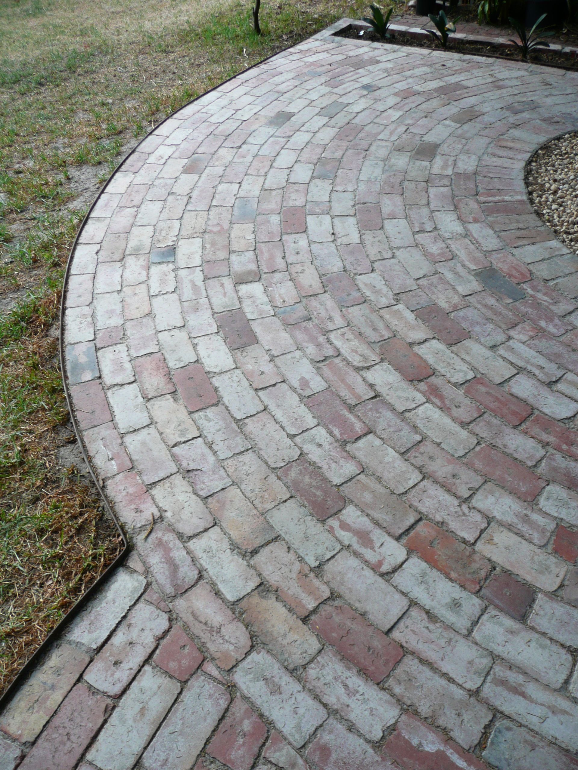 Curving brick pathway in shades of red and gray, surrounded by grass.