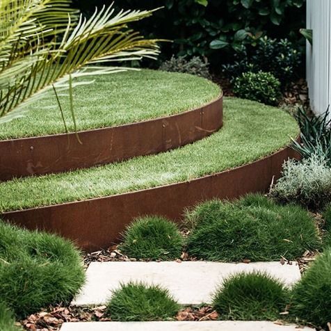 Curved, tiered lawn beds with rusty metal borders, stone path, and surrounding greenery.
