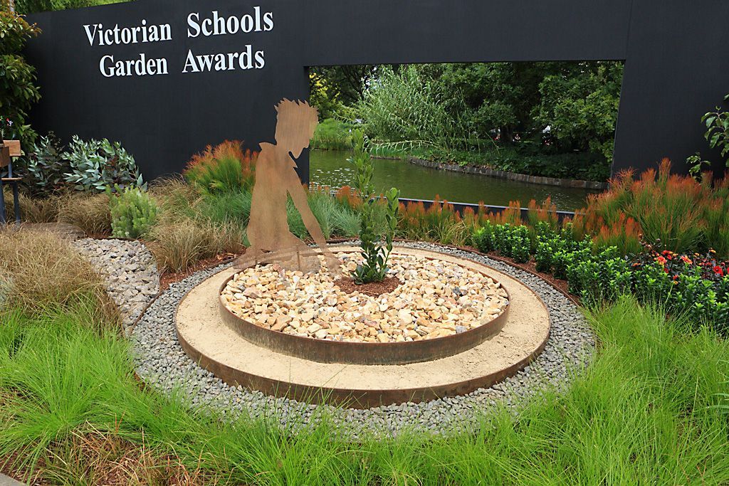 Victorian Schools Garden Awards display with metal sculpture of a child planting; garden beds, pond in background.