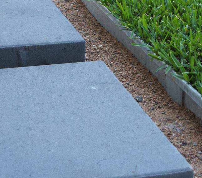 Gray pavers next to a bed of gravel and green grass.