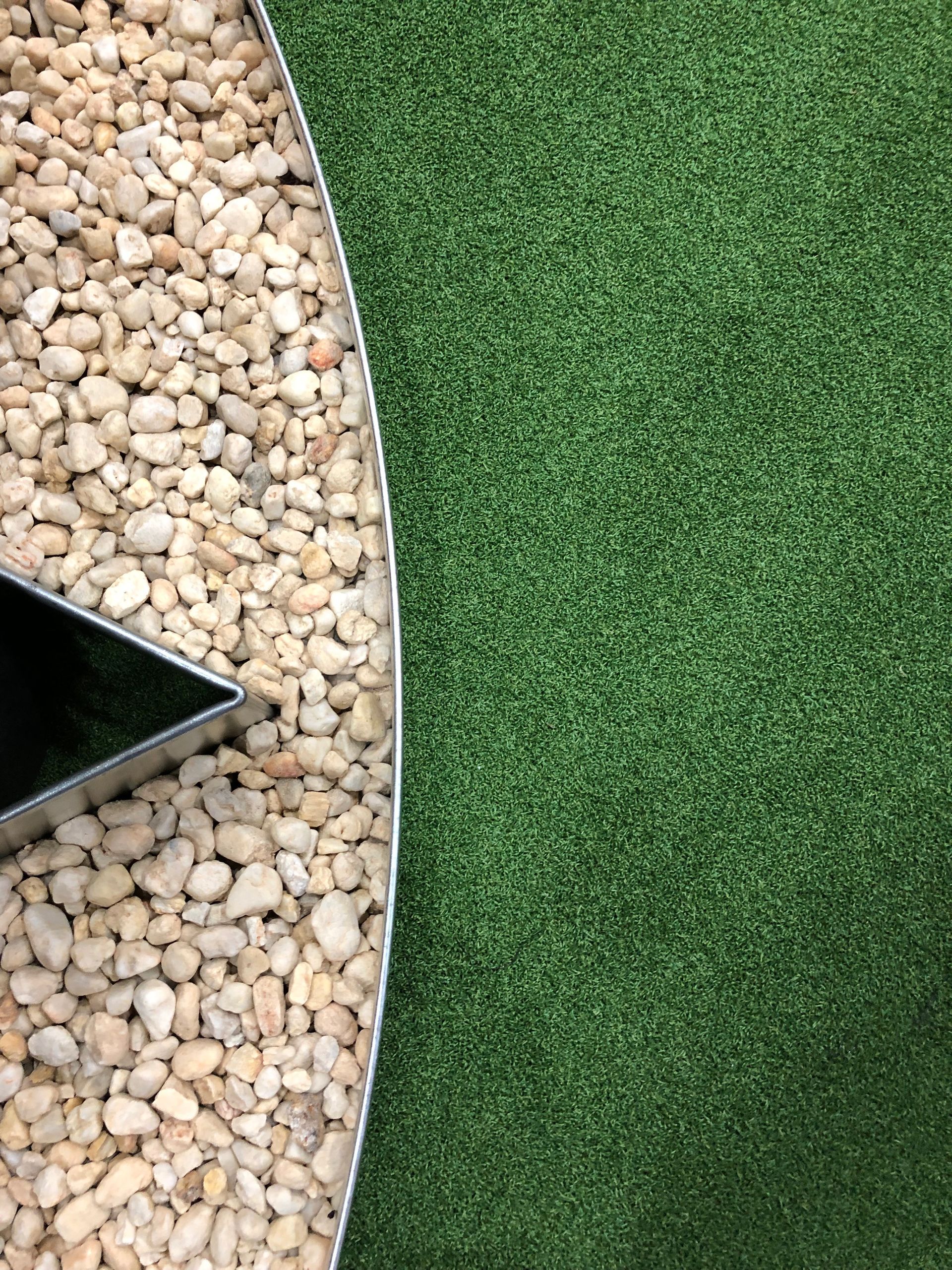 Brown pebbles border green turf, with a partial metallic star shape in the corner.