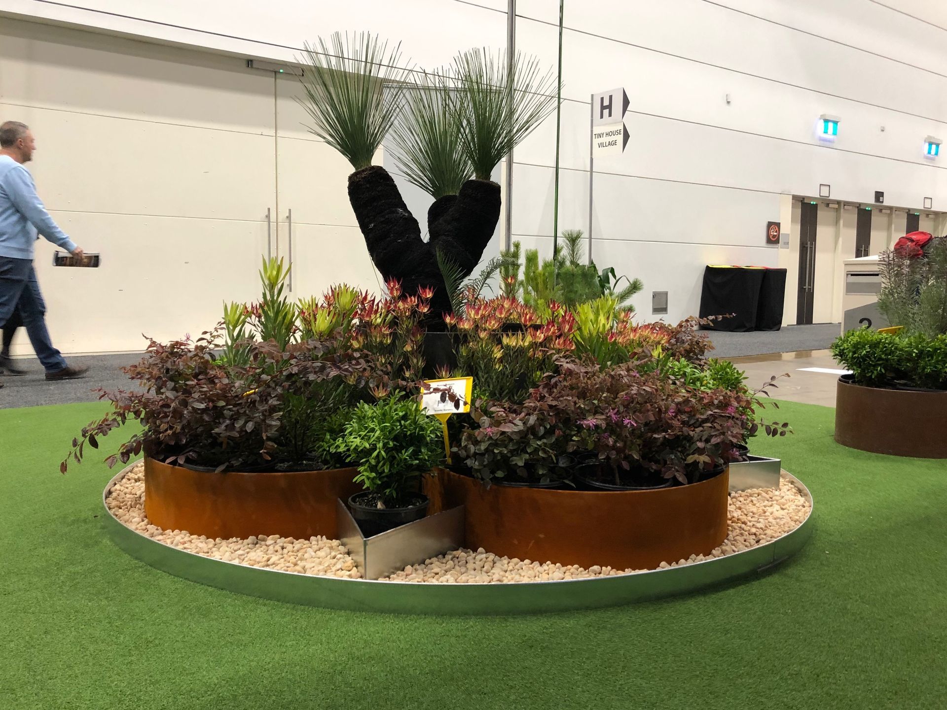 A floral display with reddish and green plants in rusty metal planters. A person walks by.