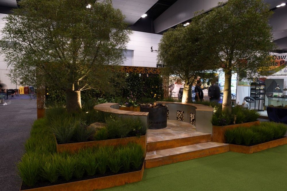 Landscaped garden display with trees, greenery, stone patio, and built-in seating.