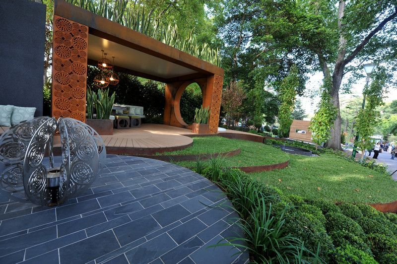 Outdoor garden with a wooden pavilion, manicured lawn, and water feature.