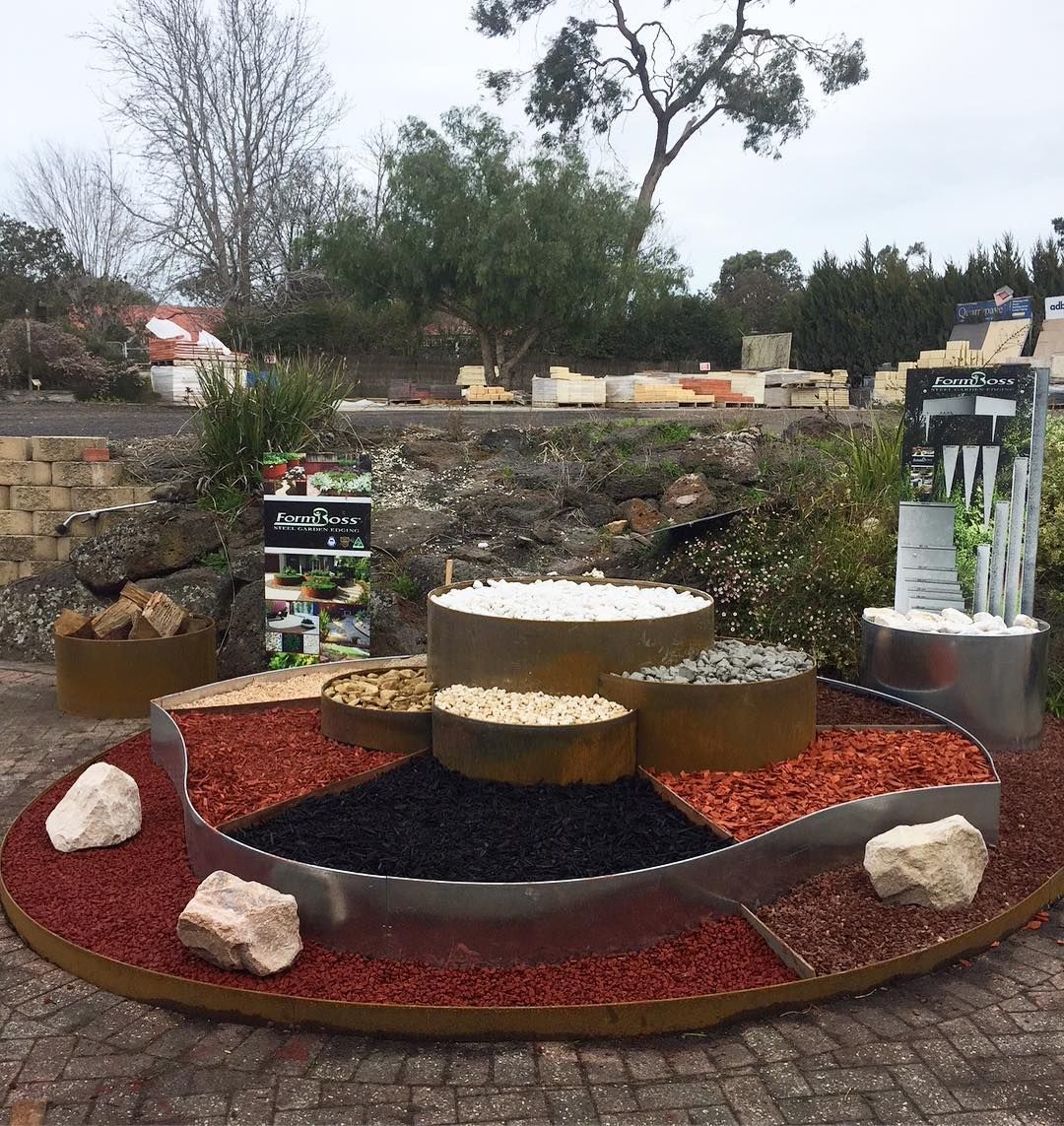 Display of landscaping materials: red, black, white, and gray stones in tiered, circular beds.
