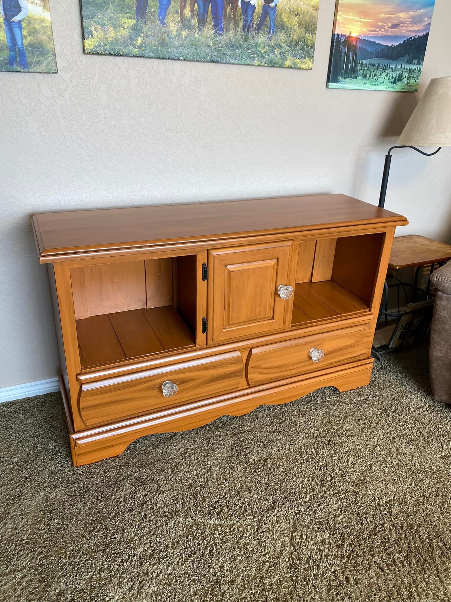 A light-brown wooden TV stand or entertainment console with two bottom drawers, one center cabinet door, and two side bays.