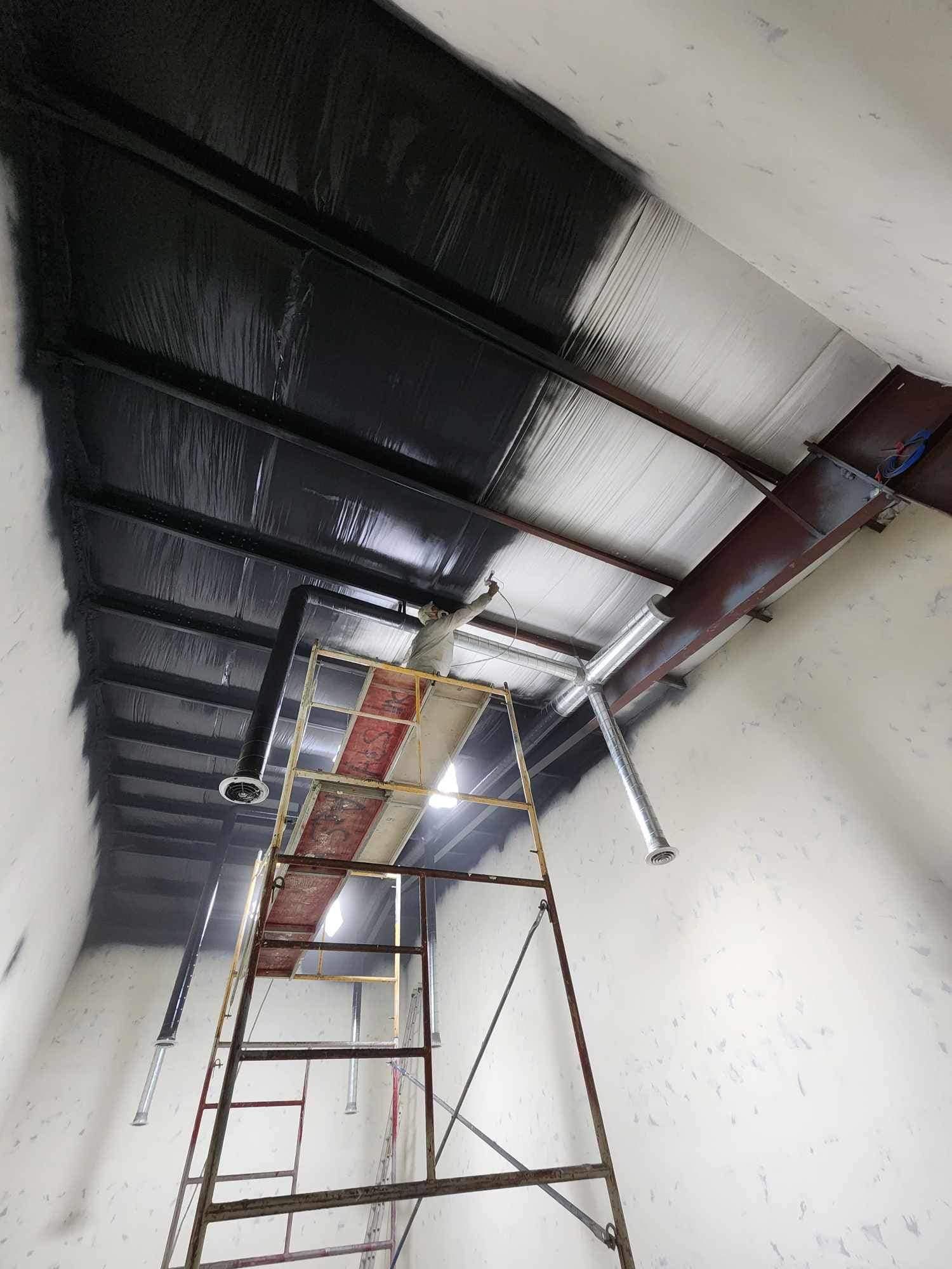 A metal scaffolding tower sits in a room with a partially painted black and silver insulated ceiling.