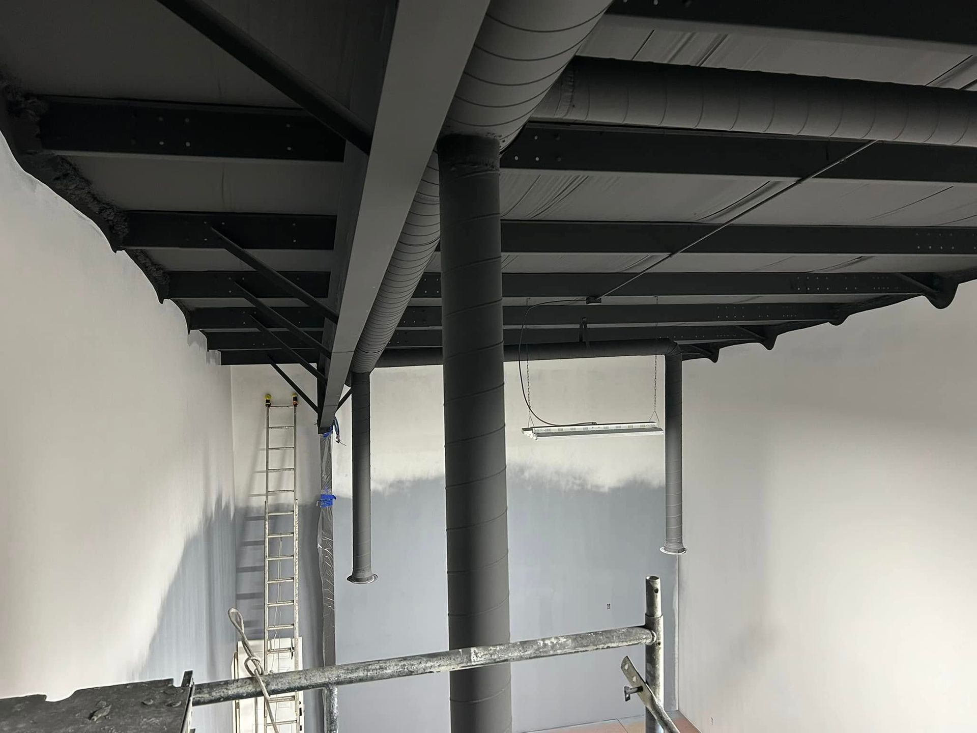 A room under renovation with dark exposed ceiling beams, cylindrical columns, white walls, and a ladder by the corner.