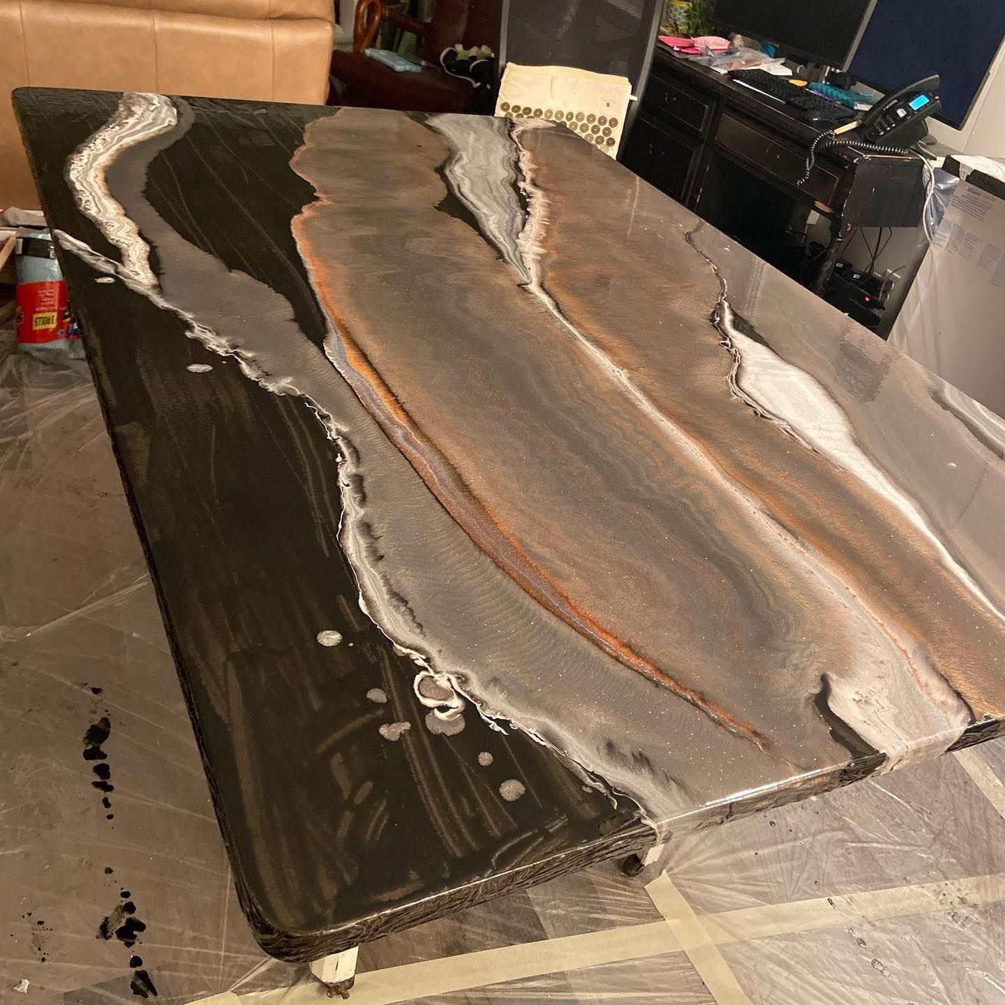 A live-edge wood table featuring a river-style resin inlay with swirling black, grey, and metallic tones.
