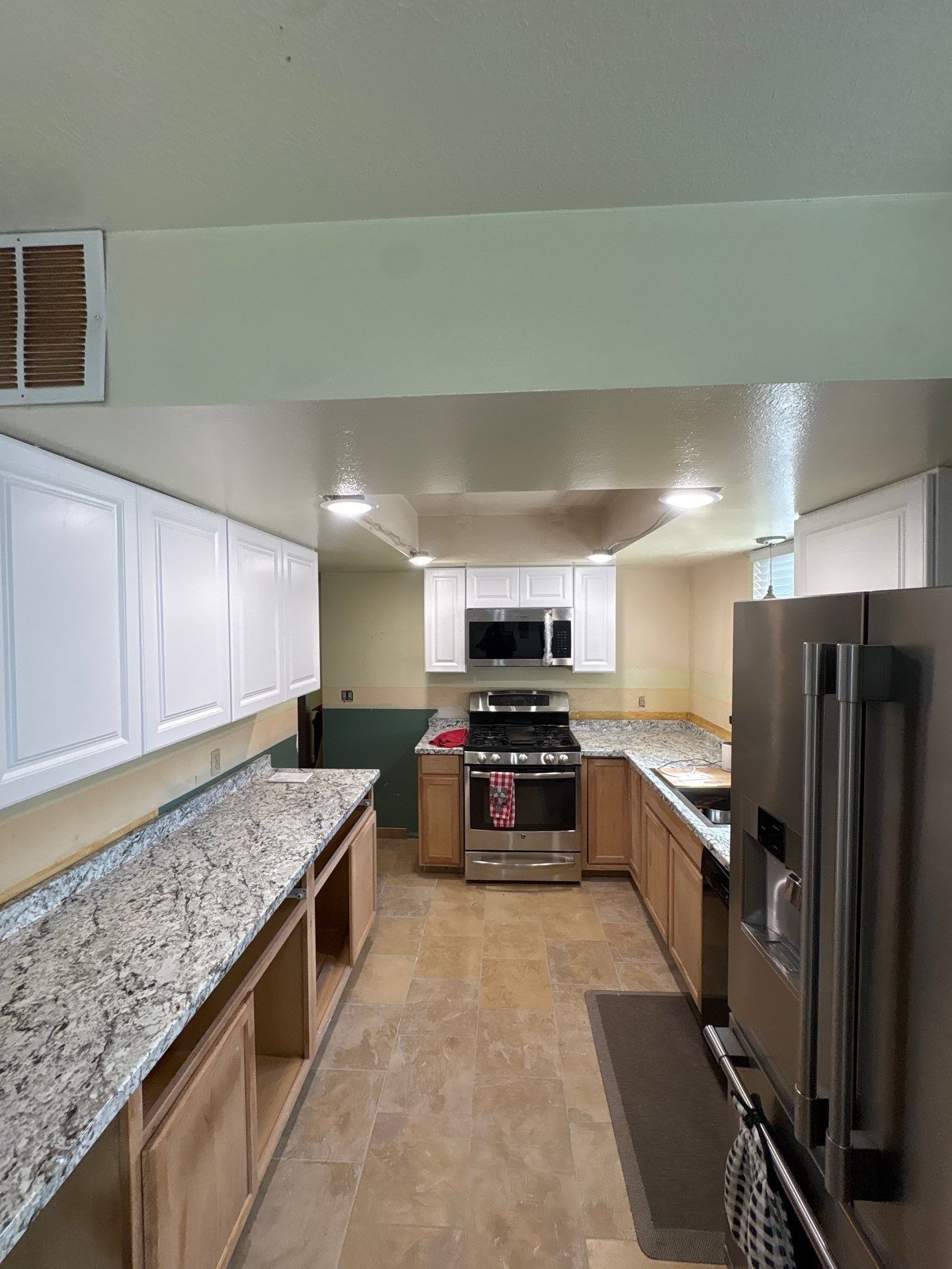 A kitchen with white upper cabinets, granite countertops over open base cabinets, a stainless steel stove, and a fridge.