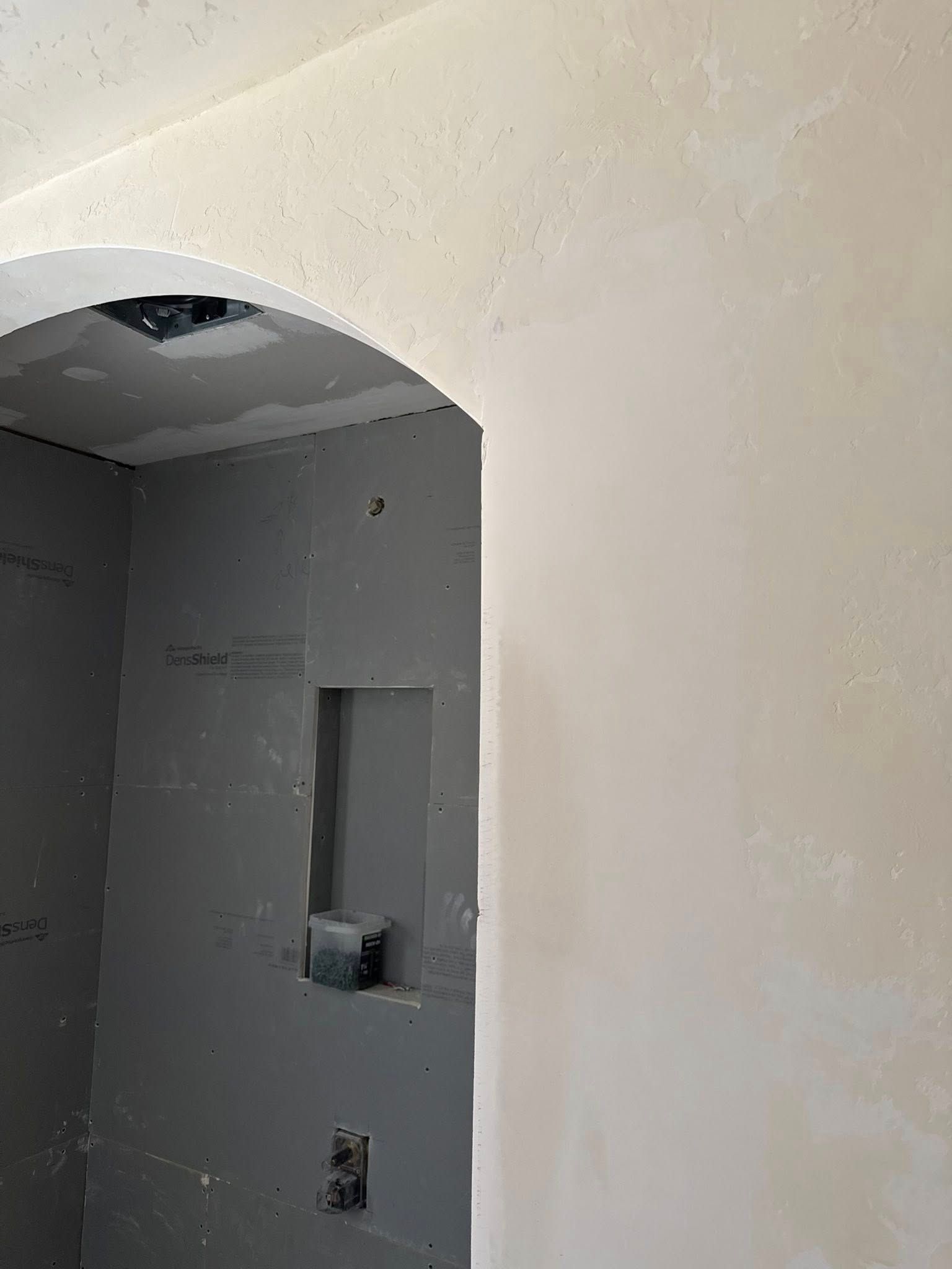 An arched doorway opening into a shower stall framed with grey cement board, featuring a built-in wall niche.