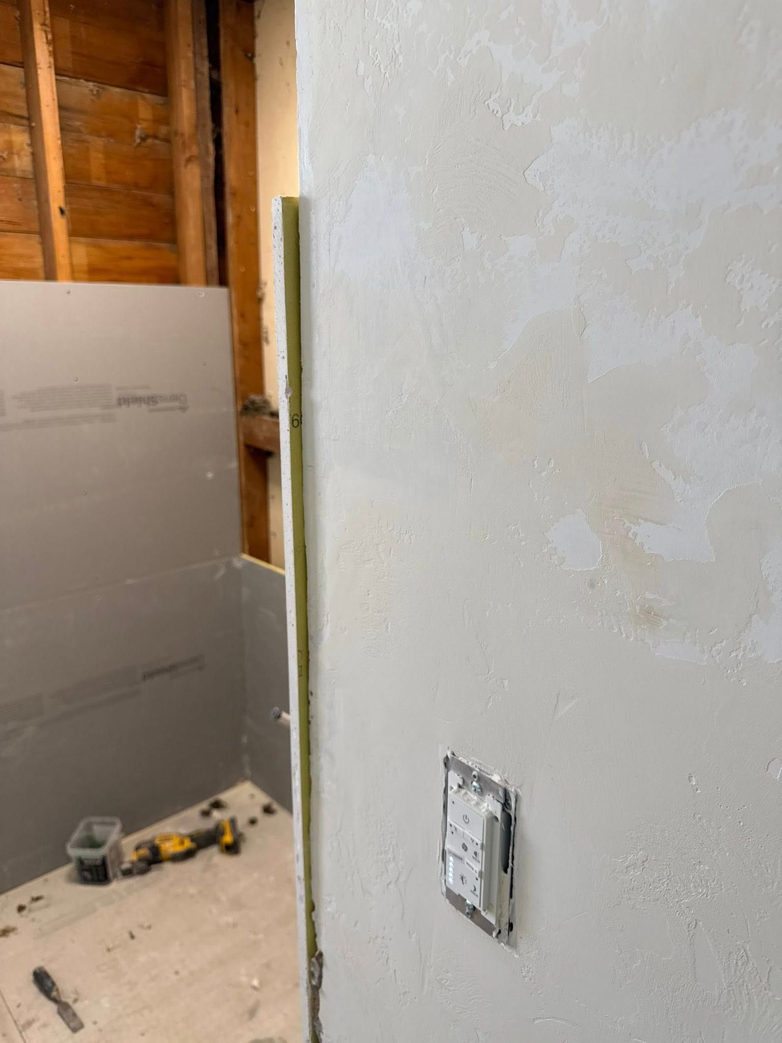 A view of a home renovation project featuring a grey drywall wall, exposed wooden wall studs, and a mounted electrical box.