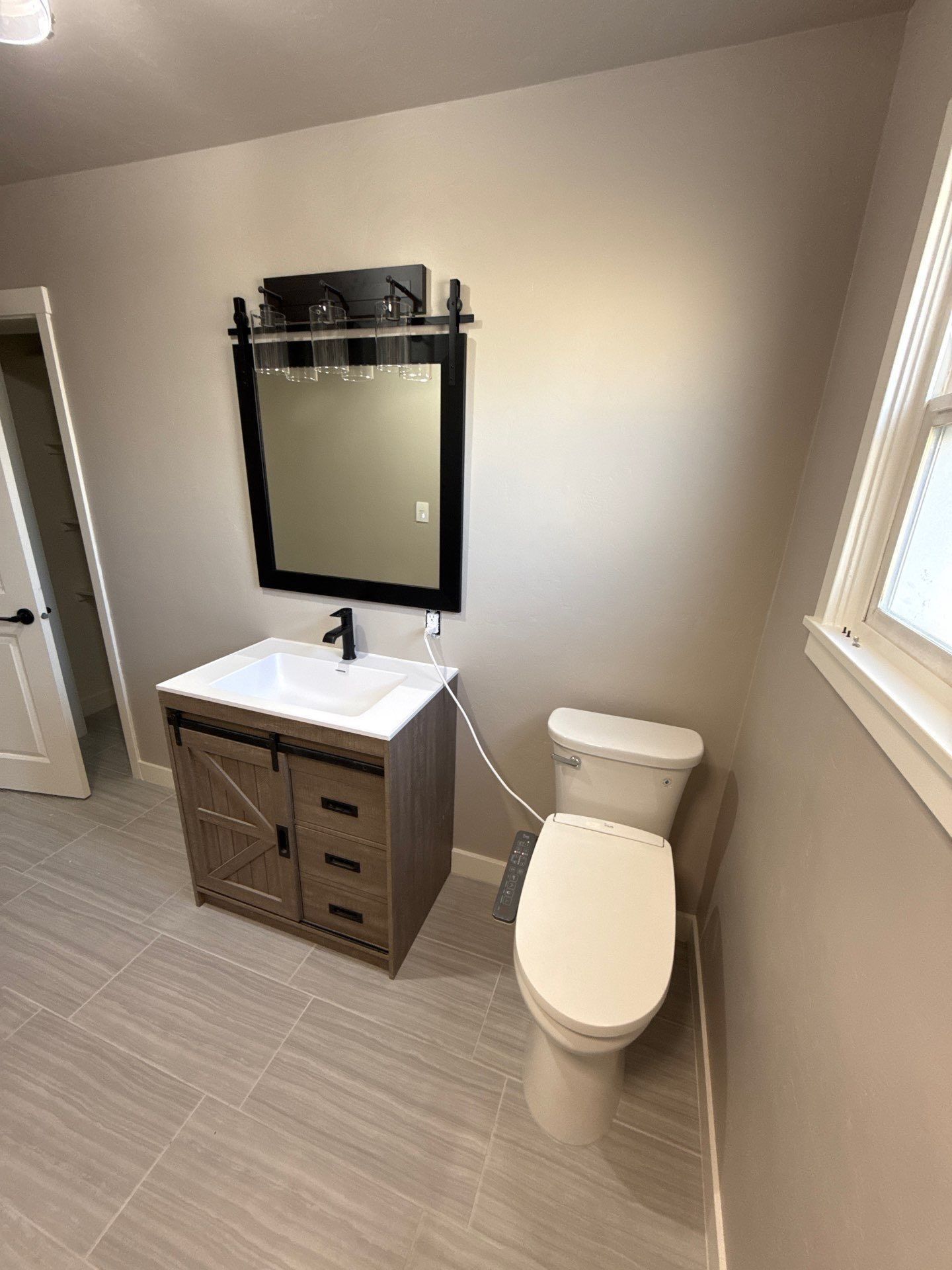 Modern bathroom with a rustic wooden vanity, black-framed mirror, white toilet, and gray tiled floor.