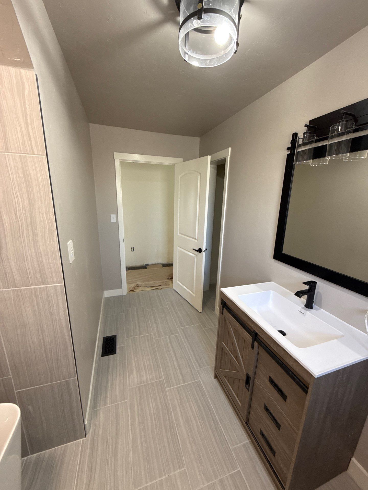 Modern bathroom with gray tiled floor, a vanity with a black-framed mirror, and an open doorway leading to another room.