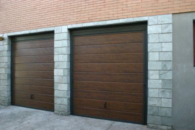 Due porte da garage in legno marrone chiuse, incastonate in un muro di pietra e mattoni.