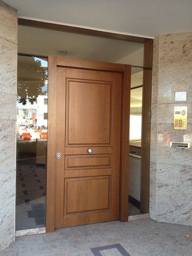 Porta d'ingresso in legno su una facciata di un edificio in pietra, con pannello del citofono accanto.