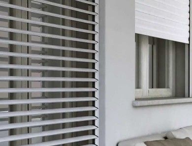 Tende da esterno grigie accanto a una parete bianca e finestra parzialmente aperta