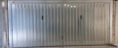Porta da garage avvolgibile in metallo con lamelle verticali, chiusa contro un muro di cemento.