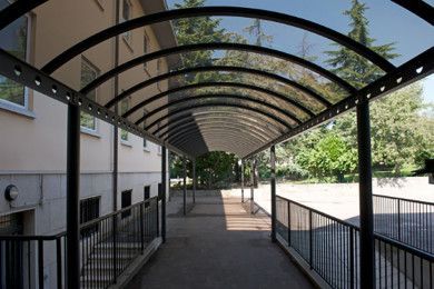 Passaggio pedonale esterno coperto con tettoia ad arco, ringhiere e un edificio su un lato.