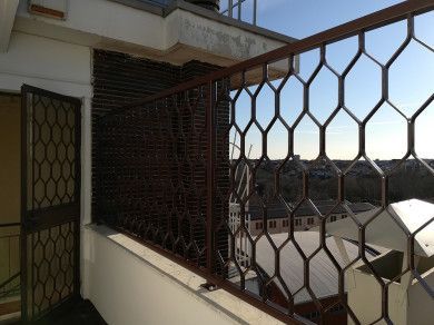 Balcone con ringhiera a traliccio marrone che si affaccia sui tetti in piena luce del giorno