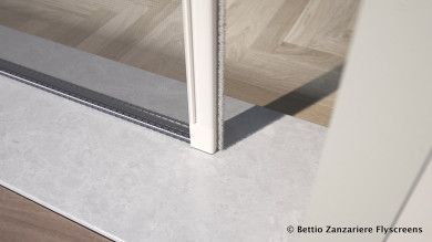 Primo piano di una porta a vetri con cornice bianca su un pavimento in legno chiaro, che mostra una soglia bassa.