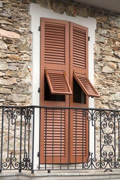 Persiane in legno chiuse e ringhiera del balcone sulla facciata di un edificio in pietra.