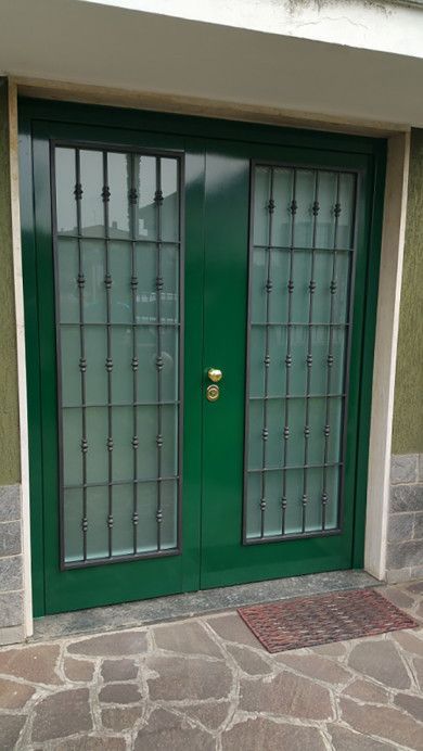 Doppia porta d'ingresso verde con pannelli in vetro e barre metalliche, incastonata in un atrio in pietra.