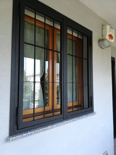 Finestra con cornice nera e sbarre metalliche su una parete esterna bianca, vista di profilo.