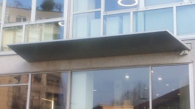 Ingresso moderno di un edificio in vetro con un'ampia tettoia nera sopra le porte.