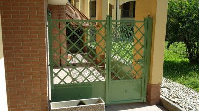 Cancello a traliccio verde accanto all'ingresso di una casa in mattoni con un piccolo gradino e un sentiero nel giardino.
