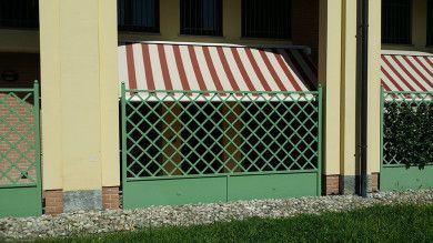 Tenda a strisce rosse e bianche sopra pannelli a traliccio verdi sulla facciata di un edificio.