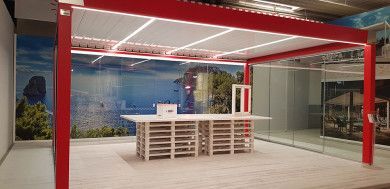 Moderna hall d'ingresso per uffici con travi rosse, bancone reception bianco e pareti in vetro che si affacciano sul verde.